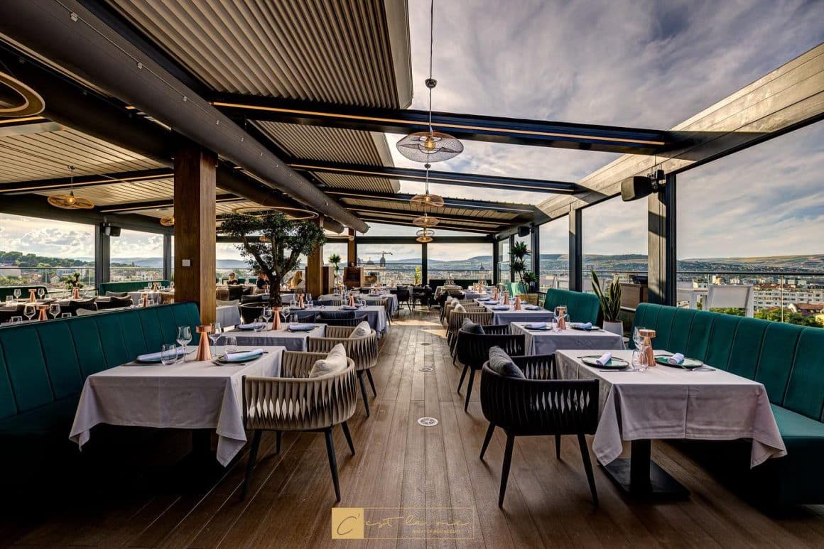 terasa panoramica de la Cest la Vie Cluj, cu mese elegante si canapele din catifea verde.