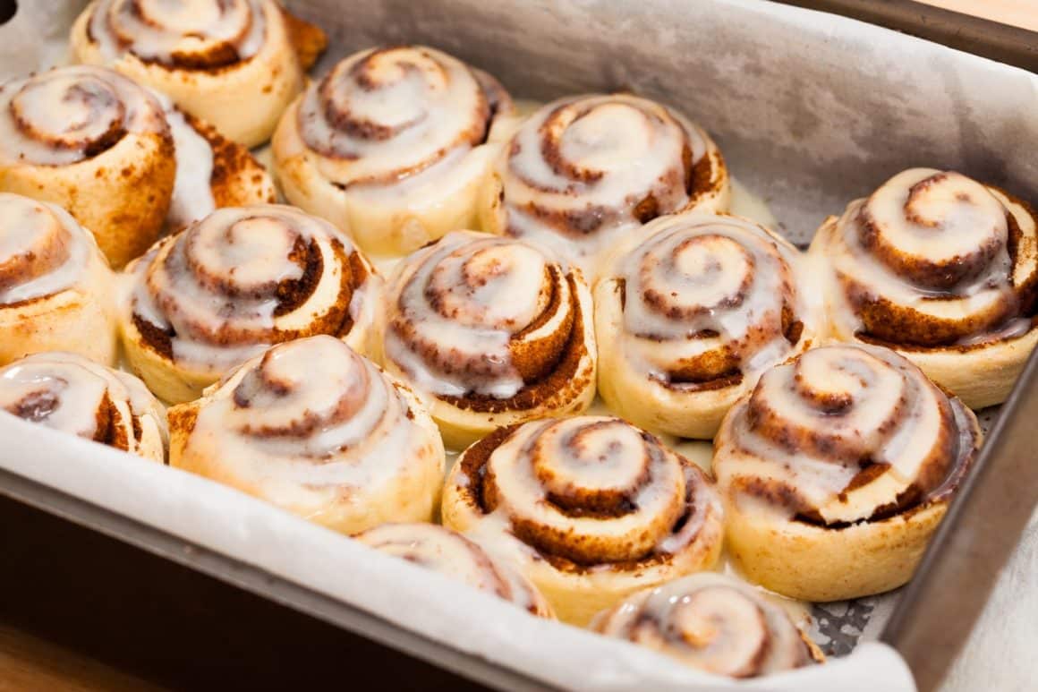 mai multe cinnamon rolss intr-o tava de copt, cu glazura deasupra