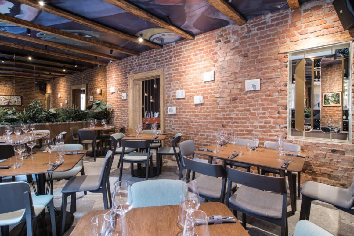 Mese elegante intr-un restaurant cu pereti din caramida aparenta si plante ornamentale, decorat elegant. Kupaj, restaurante Cluj