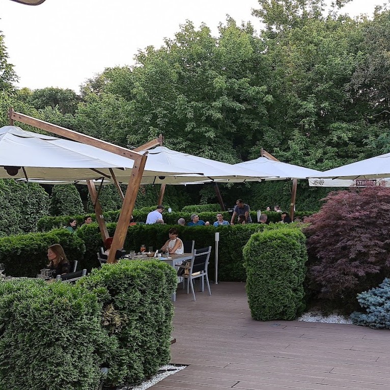 terasa de la Studio 80 din București, cu umbrele si oameni care iau masa in separeuri formate din gard viu