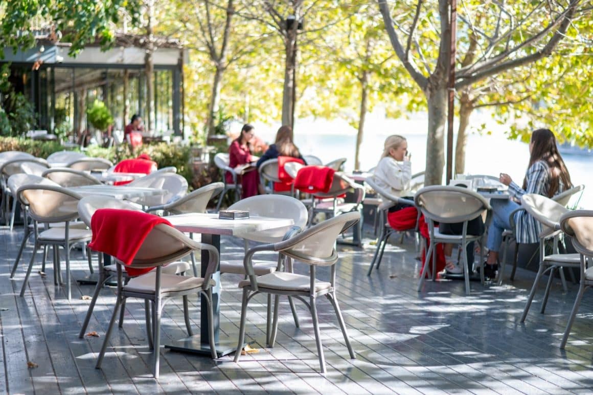 Terasa Moon Brasserie din Bucuresti, pe malul Dambovitei, cu mese amplasate pe un podet de lemn, inconjurate de copaci