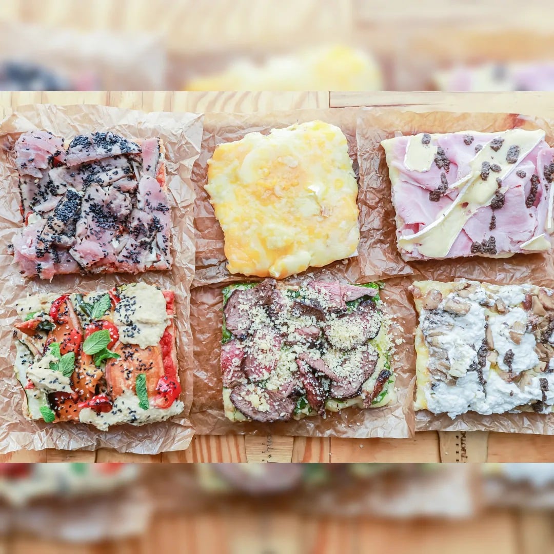 6 felii patrate de pizza pe un tocator de lemn, fiecare cu alte toppinguri