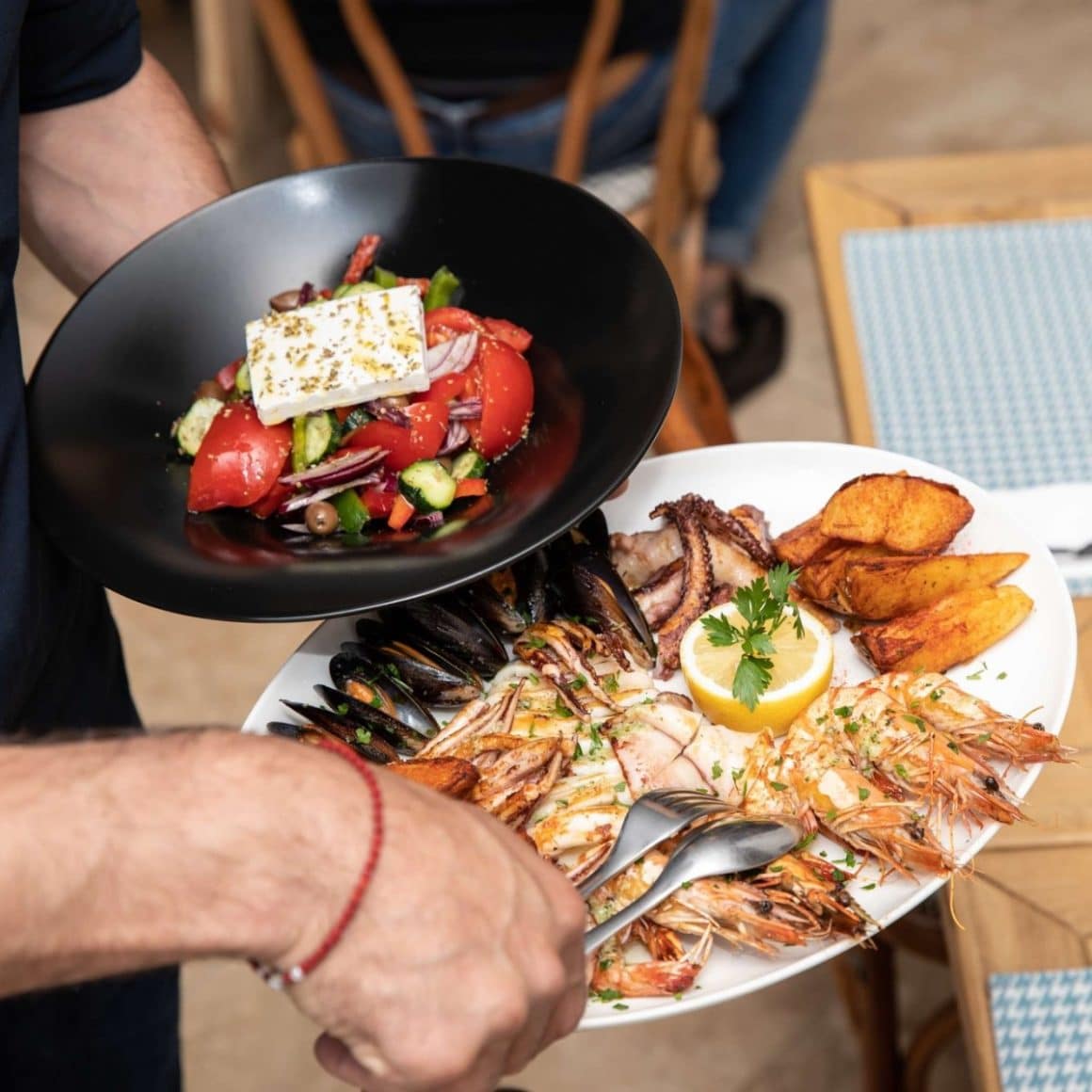 ospatar duce la masa un platou cu fructe de mare si o farfurie cu salata greceasca