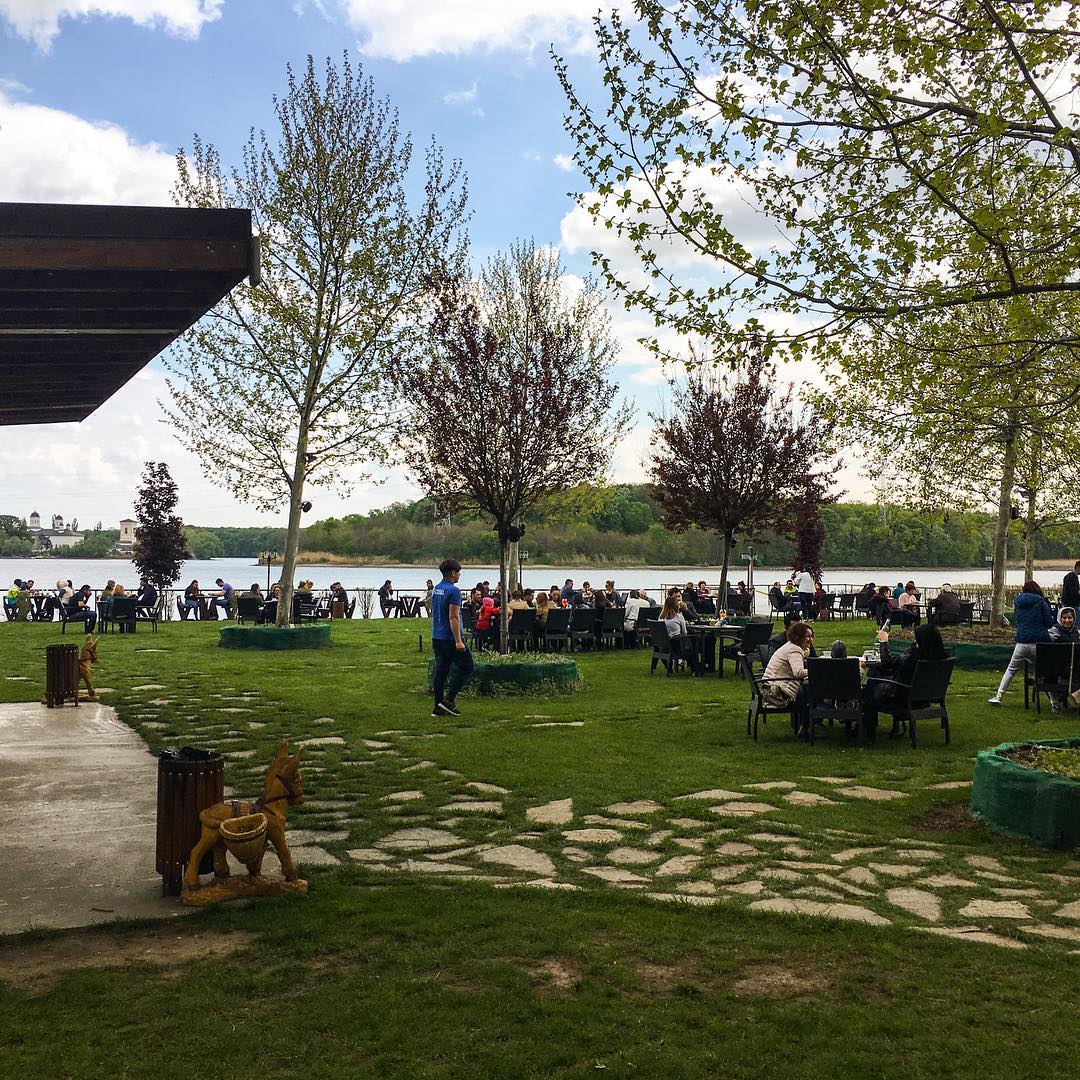 mai multi oameni iau masa pe terasa de la Restaurant cernica, unde mesele sunt asezate pe gazon. restaurante lângă București