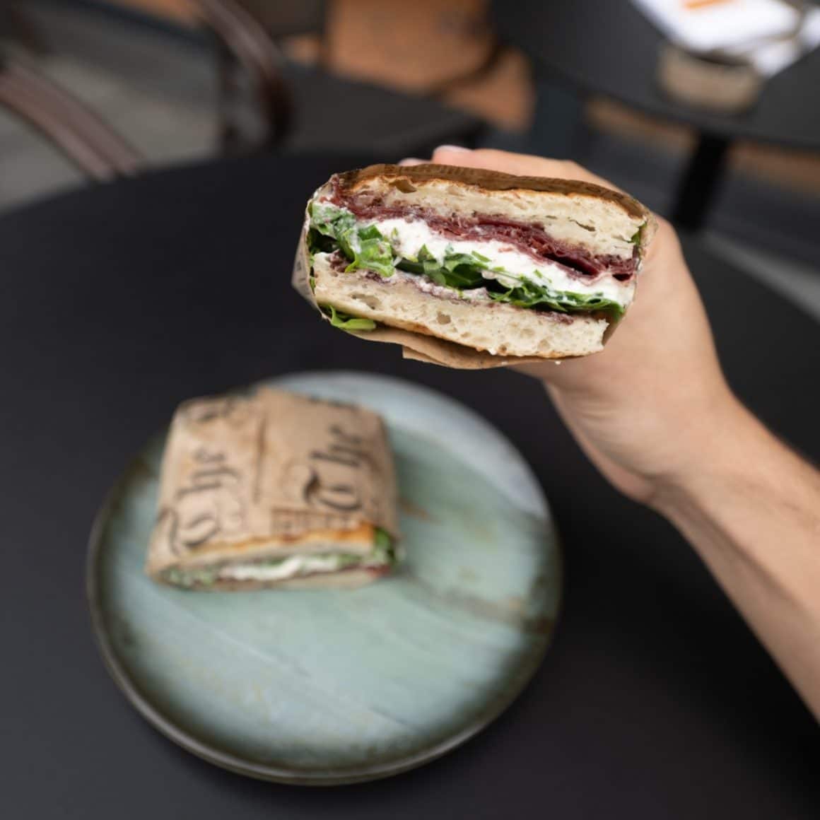 cineva tine in pana un sandviș de la Bastoni. cu branza, mezeluri si salata proaspata