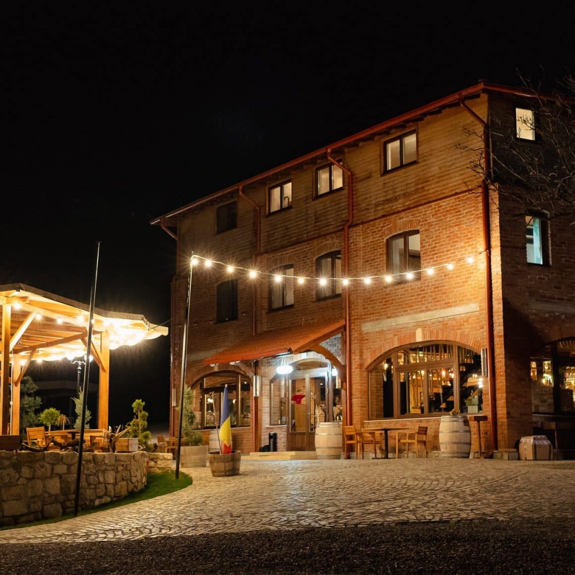 Cladirea principala de la Crama de Piatra, cu exterior din piatra aperenta si curtea luminata de beculete, fotografiata noasptea