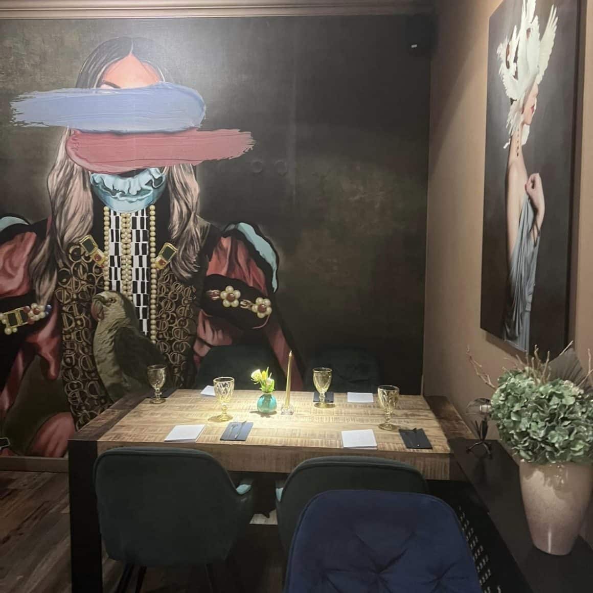 imagine din interiorul restaurantului Toujours din Iași, cu o masa in prim plan si perete cu o pictura murala in fundal. Restaurante Iași