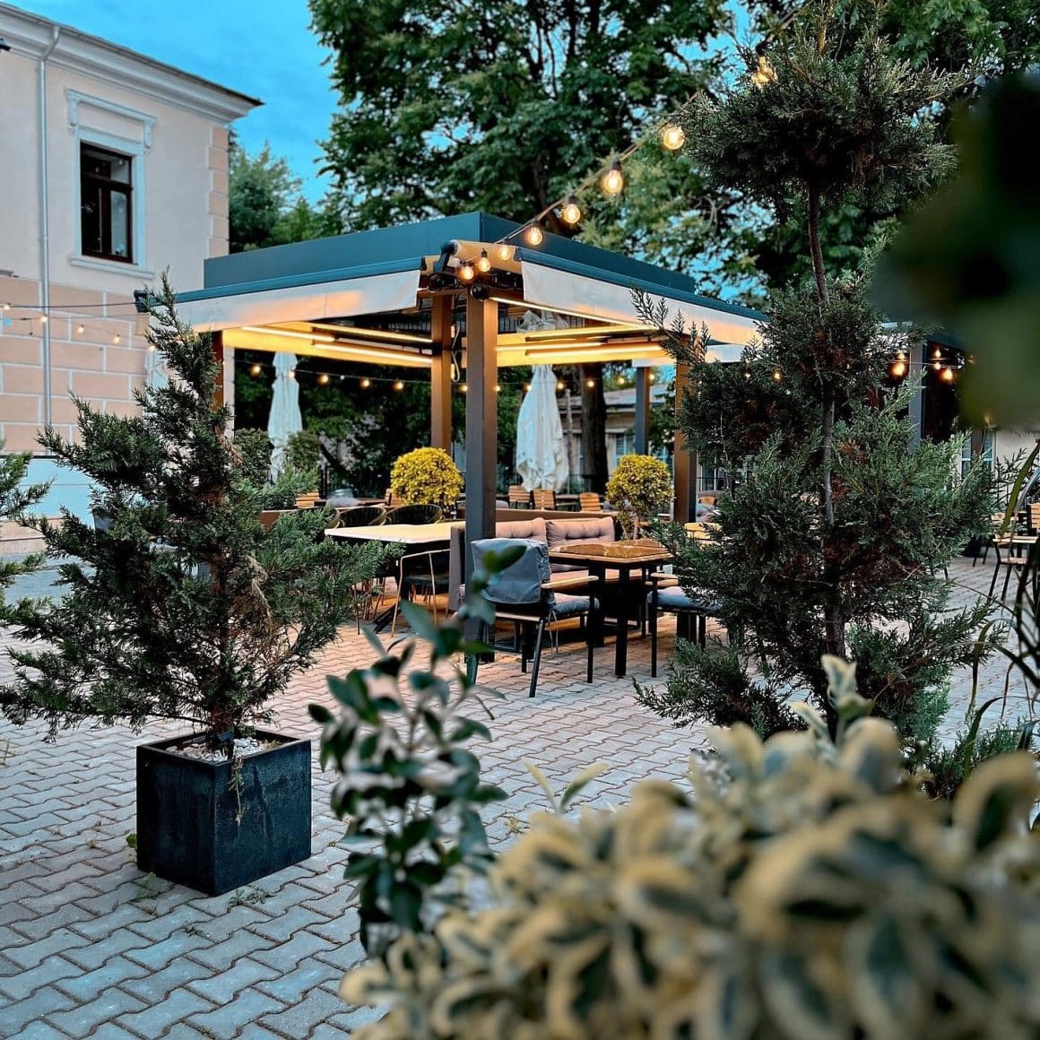 terasa restaurantului trai, cu foisoare imprejmuite de verdeata si cu beculete decoratove