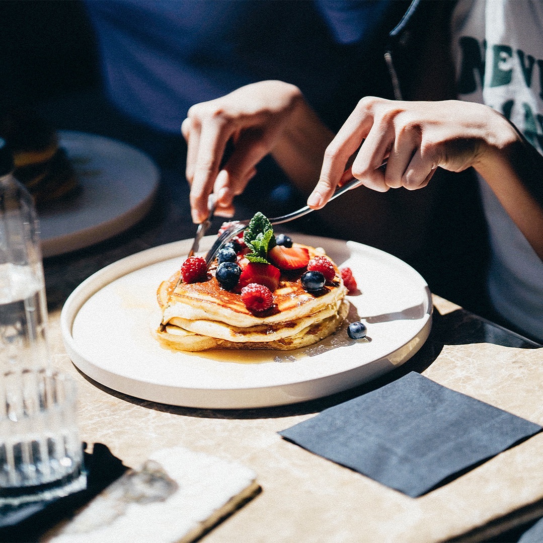 o persoane taie cu cutitul o portie de clatite americane, cu fructe de padure, la Matinee. Locuri noi București