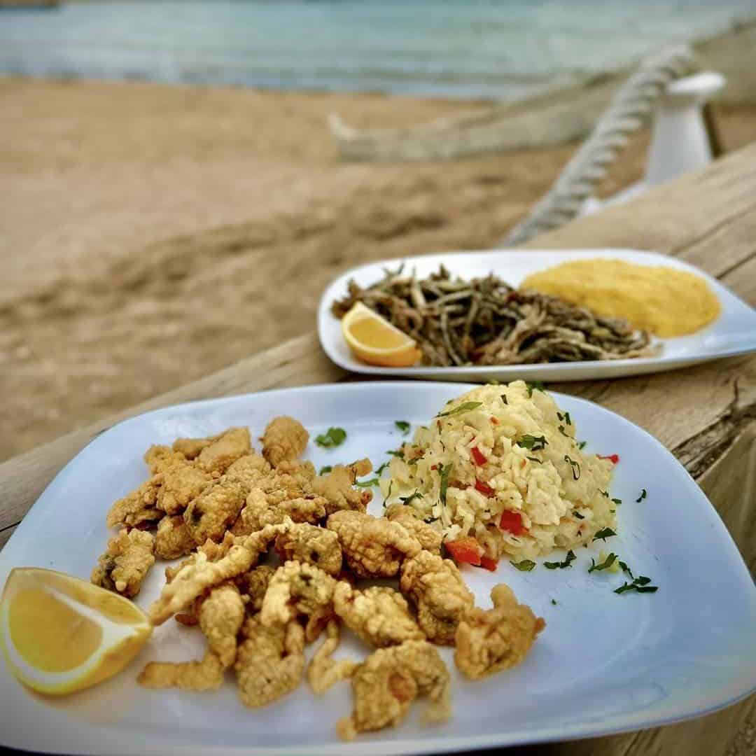fructe de mare pane cu orez si alta farfurie cu hamsii si mamaliga, iar in fundal marea si plaja de la 2 mai