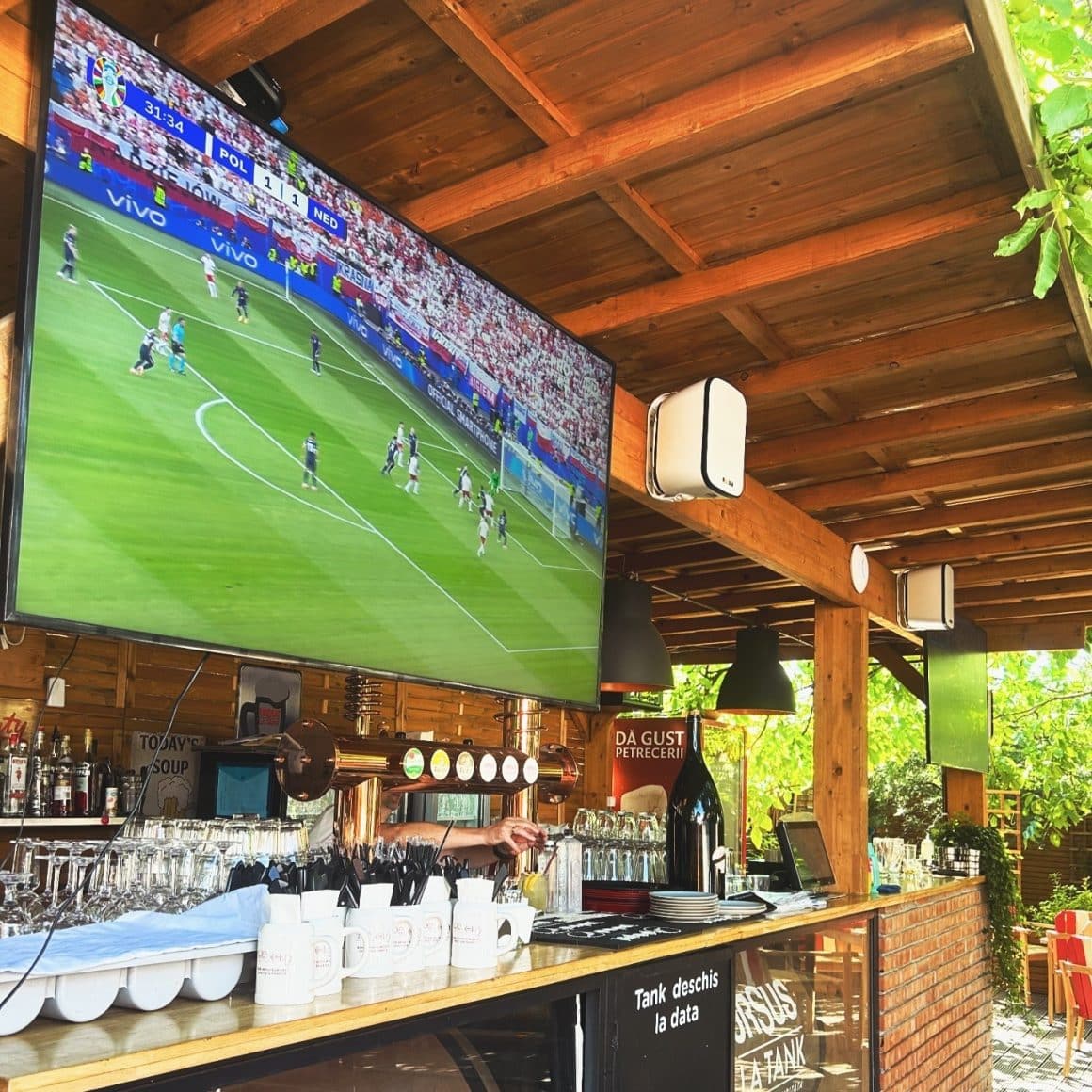un ecran mare pe care se difuzeaza un meci, in spatele barului de la Draft Pub