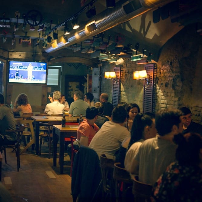 mai multi oameni la mese la Curtea Berarilor si un tv cu un meci