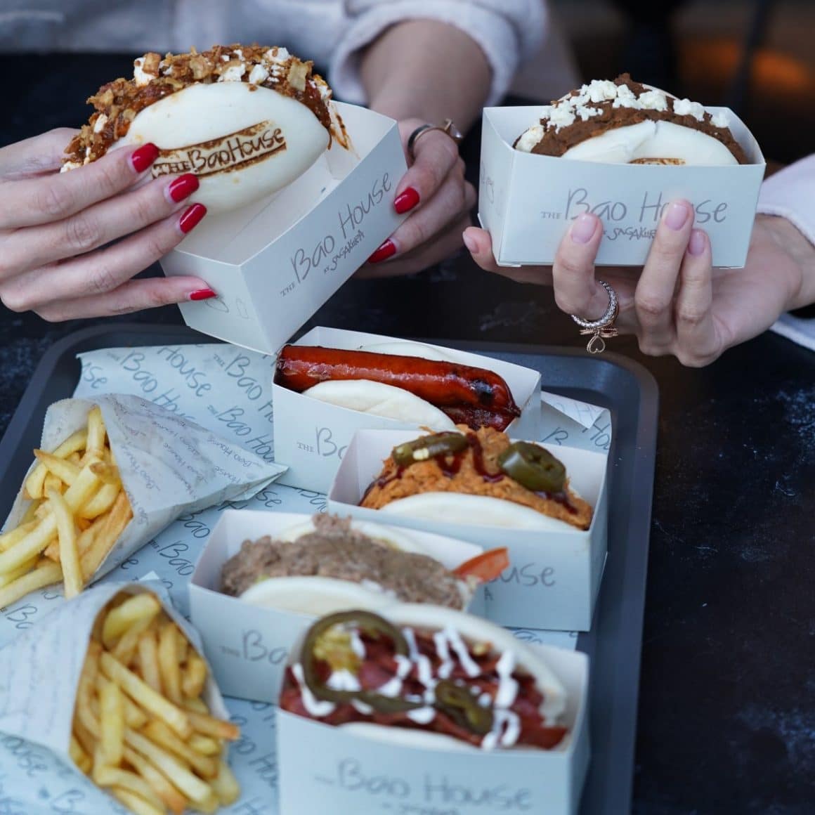 close up cu 2 fete care tin in mana bao buns, alaturi de o tava cu alte bao buns