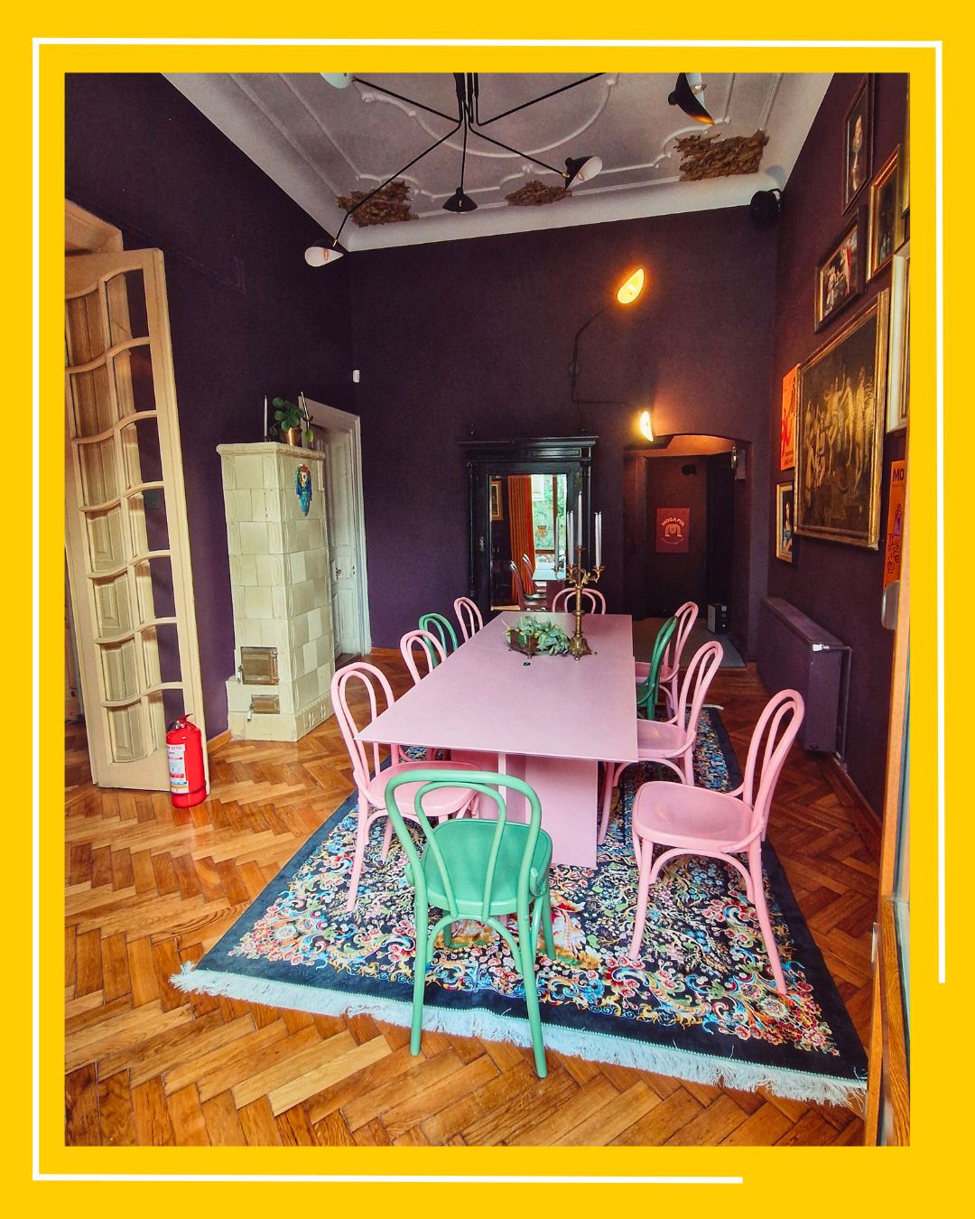 masa lunga, roz, cu scaune roz, asezata in mijlocul unei incaperi mov, cu covor persan