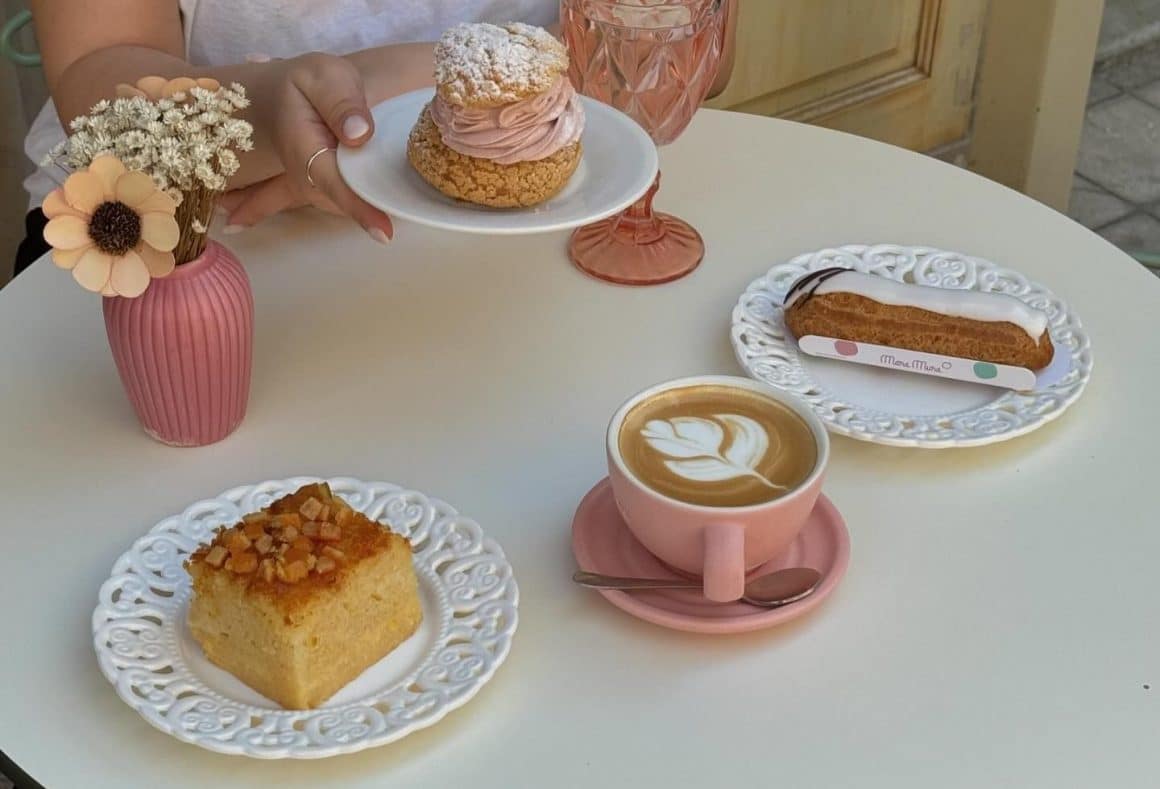 masa rotunda cu o cafea si 3 farfurii cu prajituri: choux, ecler si portokalopita în București, la Mara Mura