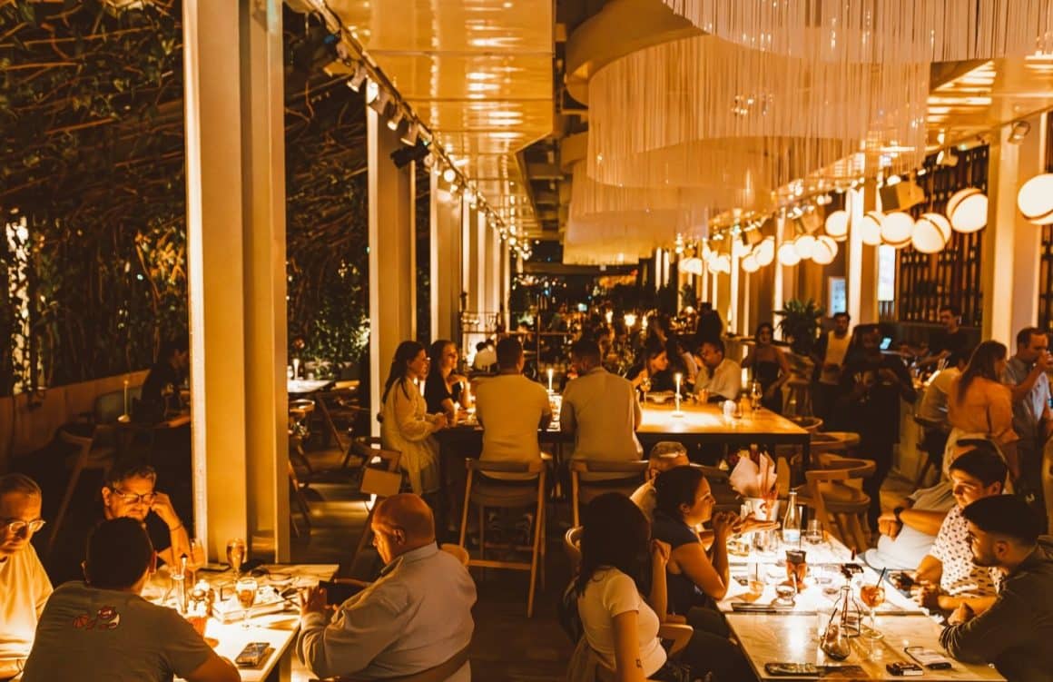 mai multi oameni iau masa la Linea Closer to the moon, seara, in spatiul cu candelabre mari si lumina calda, difuza. Oferte de Revelion de la restaurant