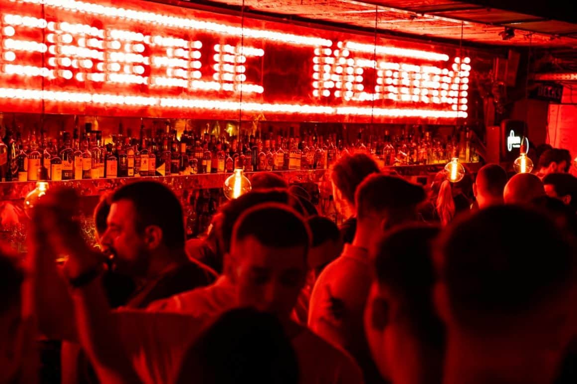 mai multi oameni la o petrecere in club Interbelic, cu lumini rosii deasupra barului, iluminat discret. Oferte de Revelion la restaurante București