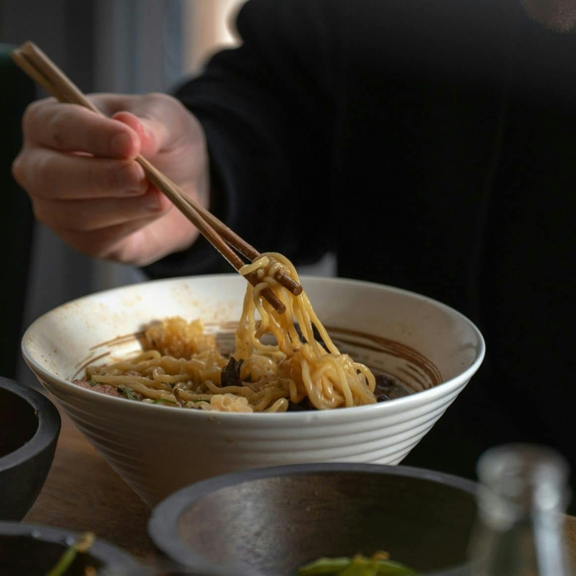o persoana manaca cu betisoare o portie de noodles japonezi