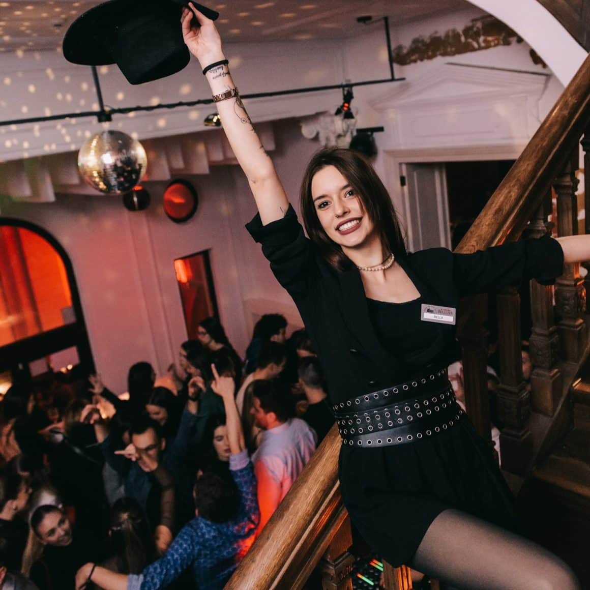 Prim plan cu o fata care saluta in aer cu o palarie, iar in fundal oameni care danseaza la La Grande Bellezza București.